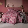 A bedroom scene with a bed dressed in a red paisley patterned duvet cover and pillows, with a gray blanket draped over the side. Produktbild-Vorschau