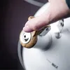 A close-up of a person's thumb pressing the lid release button on a white kettle. Podgląd zdjęcia produktu