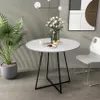 A round white dining table with black metal legs, set in a modern room with a striped wall and a white chair.