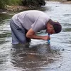 A person is in a river, using a water filter straw. Produktbild-Vorschau