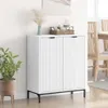 A white sideboard with fluted doors and black legs, placed against a white wall with a potted plant to the left and dining chairs visible in the background to the right. Podgląd zdjęcia produktu