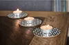 Three lit tea lights on decorative coasters on a wooden table. Podgląd zdjęcia produktu