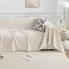 A cream-colored sofa with a throw blanket draped over it, a decorative pillow, and a cup on a saucer. Produktbild-Vorschau