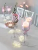 A table setting with decorative pink glass candle holders, flowers, and string lights. Náhled obrázku produktu