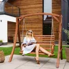 A woman is relaxing on a wooden swing in a garden setting. Náhled obrázku produktu