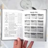A person's hand is holding open a black softcover planner, revealing the calendar pages for 2026. Produktbild-Vorschau