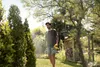 A man is using a Kärcher battery-powered pressure sprayer in a garden. Produktbild-Vorschau