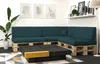 A modern living room with a sectional sofa made of pallets and dark green cushions, a dark wood coffee table with a yellow accent, a large potted plant, and framed artwork on the wall. Produktbild-Vorschau