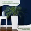 A white planter with a plant in it, next to a white side table with a vase, against a dark blue wall. Produktbild-Vorschau