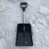 A black snow shovel with a silver handle is lying on a surface of snow. Náhled obrázku produktu