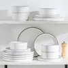 A set of white ceramic dishes with black rim lines is displayed on a white shelf. Produktbild-Vorschau