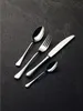 A set of four cutlery pieces, including a large spoon, a fork, a knife, and a small spoon, are arranged diagonally on a dark, textured surface. Produktbild-Vorschau
