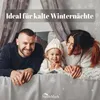A family (father, mother, and young child) lying in bed, smiling at the camera. The background has a wintery theme with snowflakes. Produktbild-Vorschau