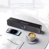 A black soundbar speaker is placed on a round table next to a smartphone, a book, and a cup of coffee. Voir les images du produit