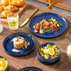 A table setting with blue ceramic plates, food, and cutlery, suggesting a meal. Produktbild-Vorschau