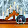 A Christmas candle arch decoration with LED candles in a window, with a snowy outdoor scene visible through the window. A circular inset shows a view from outside the window. Produktbild-Vorschau
