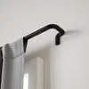 A close-up of a black curtain rod mounted on a white wall, with a grey curtain hanging from it. Podgląd zdjęcia produktu