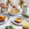 A table setting with breakfast items, including cereal, salmon, cake, and a drink, with a person serving cereal. Produktbild-Vorschau