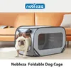 A French Bulldog stands in front of a gray foldable dog cage, with a couch and a book in the background. Produktbild-Vorschau