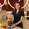 A woman in a kitchen is standing next to a blender filled with fruit. Produktbild-Vorschau