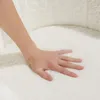A hand pressing into a soft, white, fluffy surface, likely a cushion or upholstery. Produktbild-Vorschau