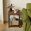 A square side table with a wooden top and metal frame, placed next to a green sofa. The table has a vase of flowers, a small radio, and a candle on top, and a basket of magazines on the lower shelf. Produktbild-Vorschau