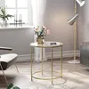 A round glass coffee table with a gold frame is placed next to a chair in a well-lit room. Náhľad obrázku produktu