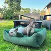 Two French Bulldogs relaxing in a green dog bed on a grassy lawn, with outdoor furniture and a house in the background. Náhled obrázku produktu