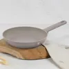 A gray frying pan is placed on a wooden cutting board, with a beige cloth and wheat stalks in the foreground. Produktbild-Vorschau