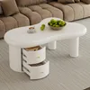 A white coffee table with two open drawers, placed on a rug in front of a sofa. Voir les images du produit