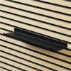 A black shelf mounted on a slatted wooden wall. Produktbild-Vorschau