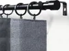 A close-up view of a black metal curtain rod with rings and gray fabric curtains. Produktbild-Vorschau