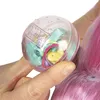 A hand holding a clear plastic ball containing small toys and accessories, next to a doll's pink hair. Podgląd zdjęcia produktu