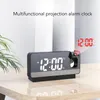 A digital alarm clock with projection capabilities sits on a wooden table, displaying the time and projecting the time onto a wall. Anteprima dell’immagine prodotto