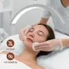 A woman is receiving a facial treatment under a crescent-shaped LED light. Produktbild-Vorschau