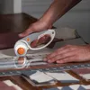 A person is using a rotary cutter to cut fabric on a wooden table. Produktbild-Vorschau