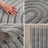 A collage of four close-up images of a gray shaggy rug with a ribbed texture, showing different angles and details of the material and design. Voir les images du produit