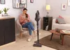 A woman is sitting in a chair and using her phone while a vacuum cleaner stands next to her. Voir les images du produit
