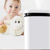A baby is lying next to a stuffed sheep and a white humidifier. Voir les images du produit