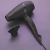 A black hairdryer with a purple accent and a nozzle attachment rests on a purple textured surface. Náhled obrázku produktu