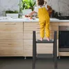 A young child in yellow overalls stands on a black two-step ladder in a kitchen, reaching for strawberries in a bowl on the counter. Náhled obrázku produktu