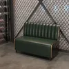 A green sofa with gold trim sits in front of a textured wall and a metal grate. Anteprima dell’immagine prodotto