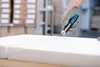 A hand wearing a glove is using a utility knife to cut a white material in a warehouse setting. Voir les images du produit