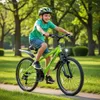 A young boy is riding a green bicycle on a paved path in a park. Produktbild-Vorschau