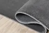 A close-up view of a gray rug rolled up, showing its textured surface and non-slip backing, placed on a wooden floor. Produktbild-Vorschau