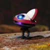 A small, futuristic robot with blue glowing eyes sits on a rocky, outdoor surface. Anteprima dell’immagine prodotto