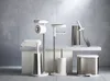 A collection of modern bathroom accessories, including toilet paper holders, a toilet brush, and a trash can, arranged on a light-colored surface against a tiled wall. Voir les images du produit
