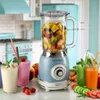 A vintage-style blender filled with fruit, surrounded by smoothies and fresh produce, in a kitchen setting. Anteprima dell’immagine prodotto