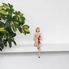 A decorative figurine of a woman in a red swimsuit sitting on a shelf next to a plant. Anteprima dell’immagine prodotto