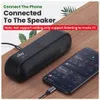 A black speaker is connected to a smartphone via an aux cable, both resting on a wooden surface with some greenery in the background. Anteprima dell’immagine prodotto
